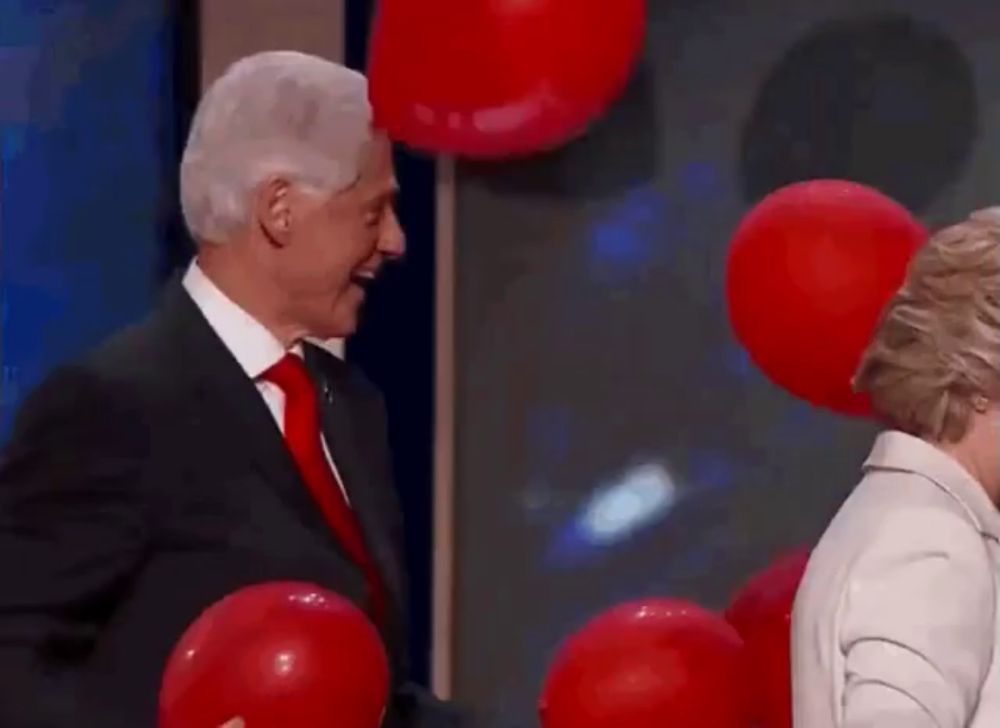 a man in a suit and tie is standing next to a woman with red balloons on her face