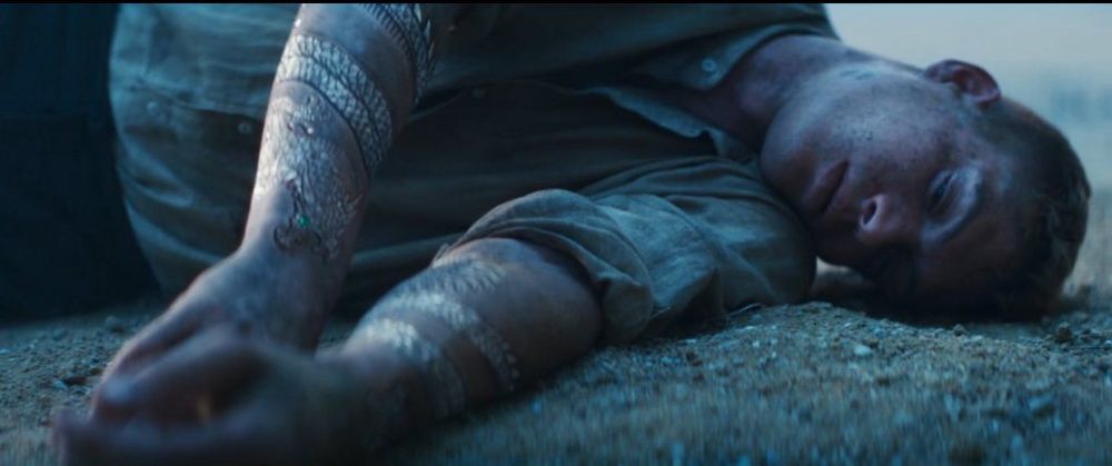 Rand al'Thor lying unconscious on the ground, with both arms showing his new golden dragon tattoos coiled around both forearms