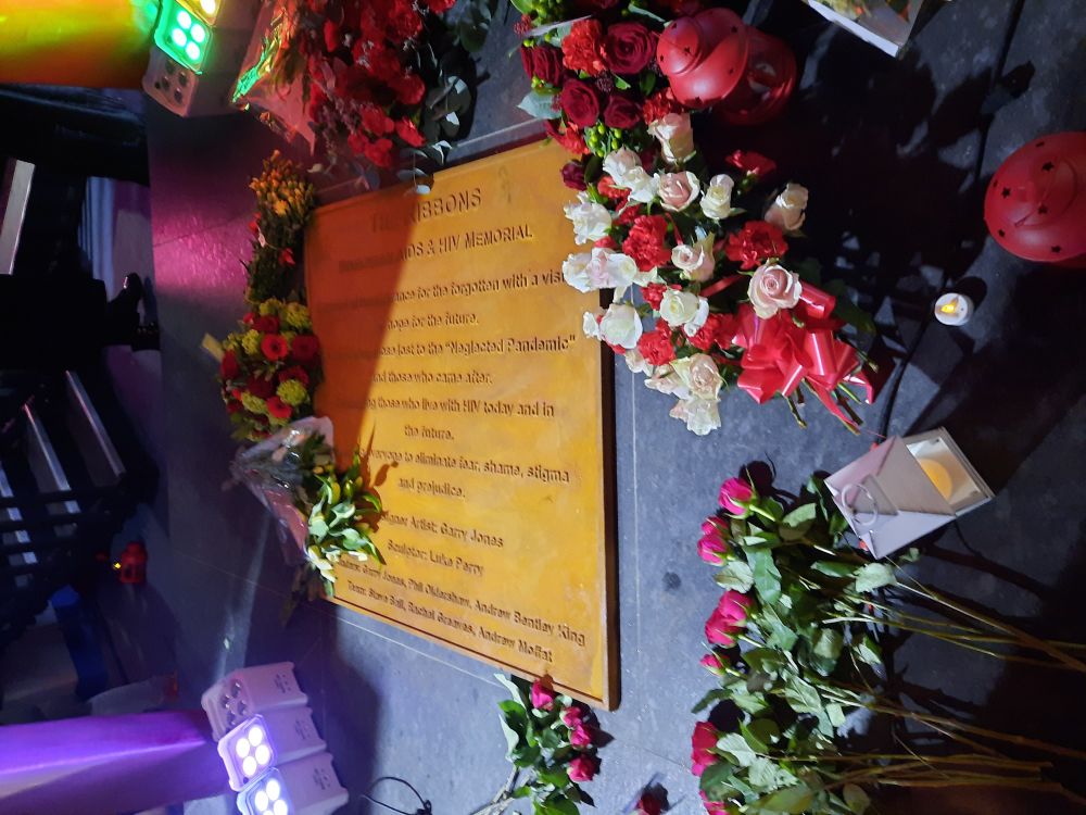 The plaque beneath the memorial which explains who created it, wreathes of flowers have been lain on it