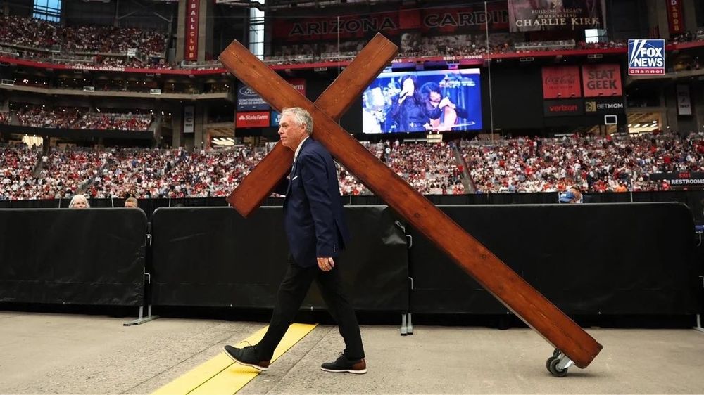 Man carrying a massive wooden cross with wheels at the bottom at Charlie Kirk's rememberance.