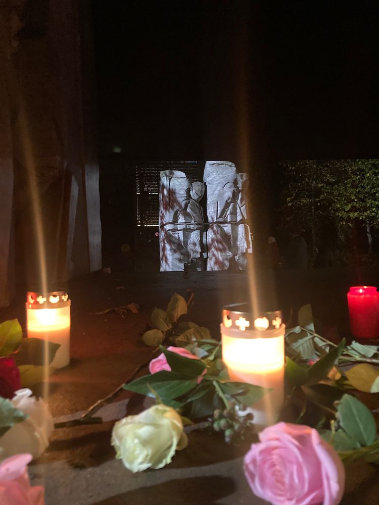 Vordergrund: Kerzen, Rosen. Hintergrund: Teile des Denkmals