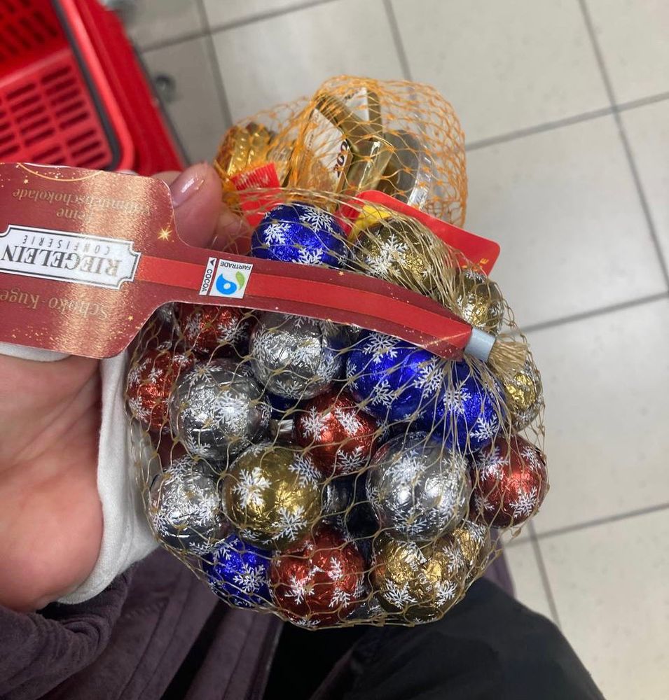 Billigschokolade-Kugeln in buntem Stanniolpapier mit Schneeflocken im Netz in einer Hand