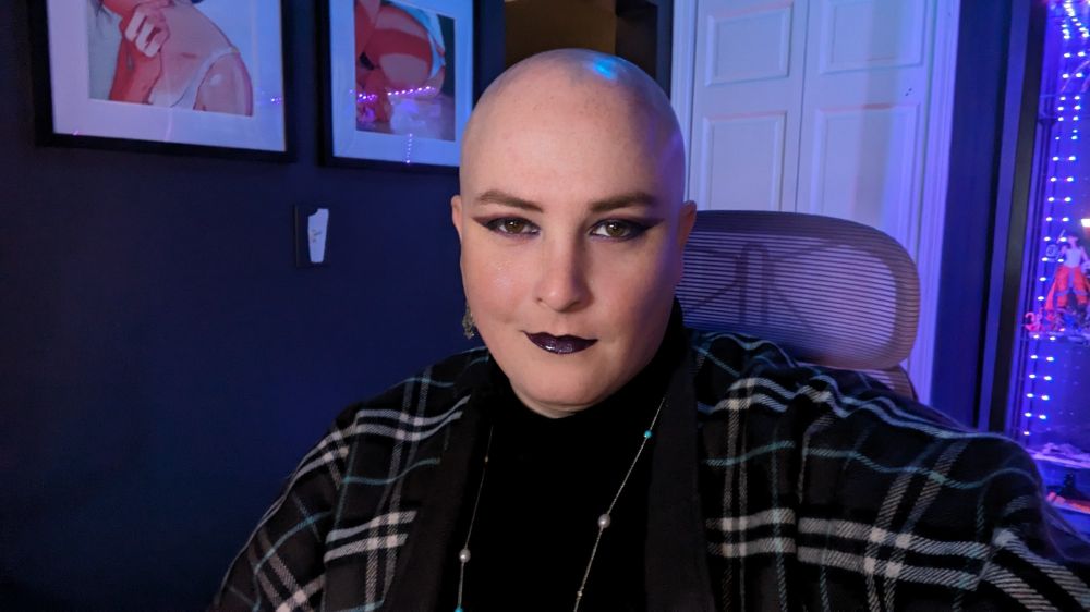 Jaina smiling looking to camera. She's wearing dark eyeshadow and lipstick and a dark cape with white and teal accents