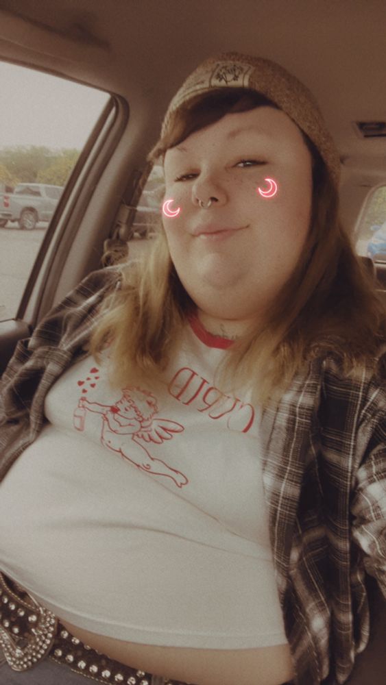 Vicci in a white shirt, jeans, and a black flannel overshirt. Shot from a low angle, her hair is down and adorned with a brown beanie. 