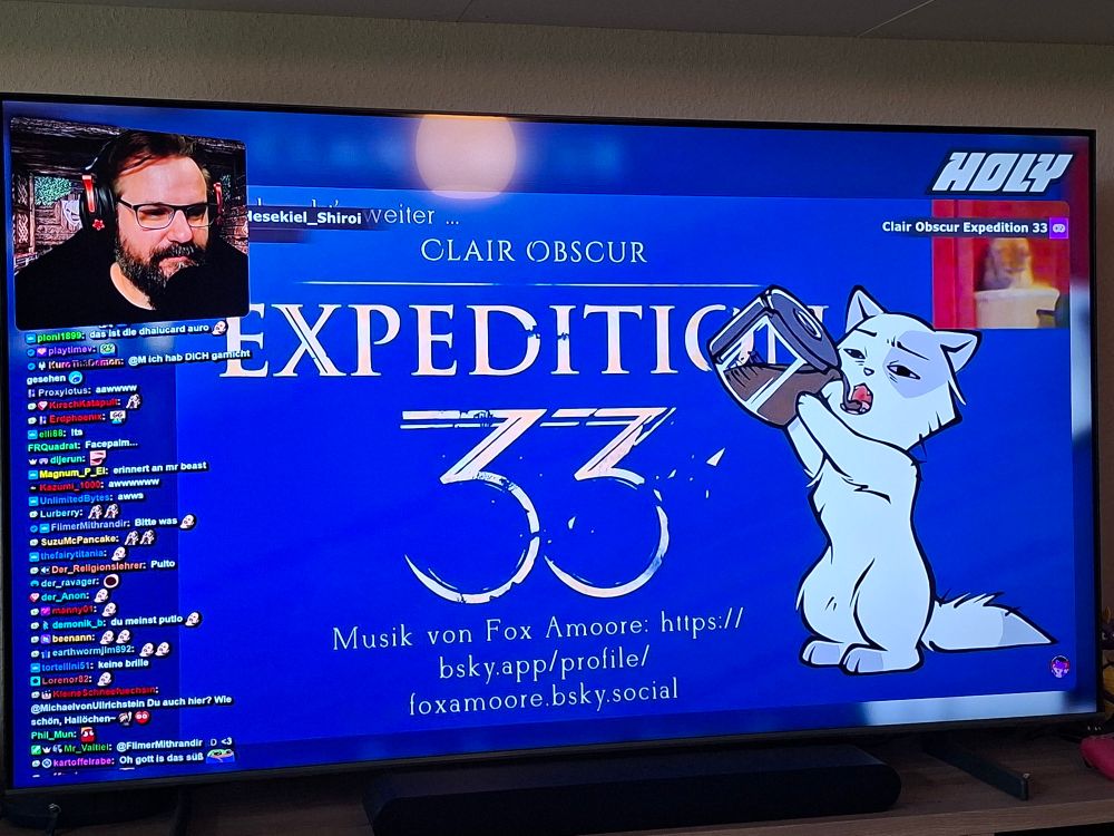 Foto con meinem Fernseher. Zu sehen ist ein Ausschnitt aus einem React-Video von Gronkh der Stream-Clips-Germany schaut. Hier ist in diesem Moment ein Clip aus einem von Pans Streams zu sehen in dem Sie Expedition 33 spielt während in einem kleinen Bildauschnitt in der rechten oberen Ecke ihre Katze beim Kotzen zu sehen ist.