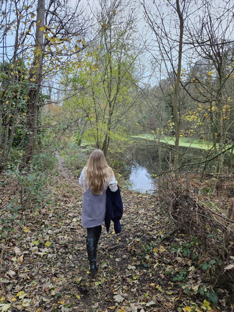 A photograph of me, taken from behind, as I walk along a wooded path by a lake