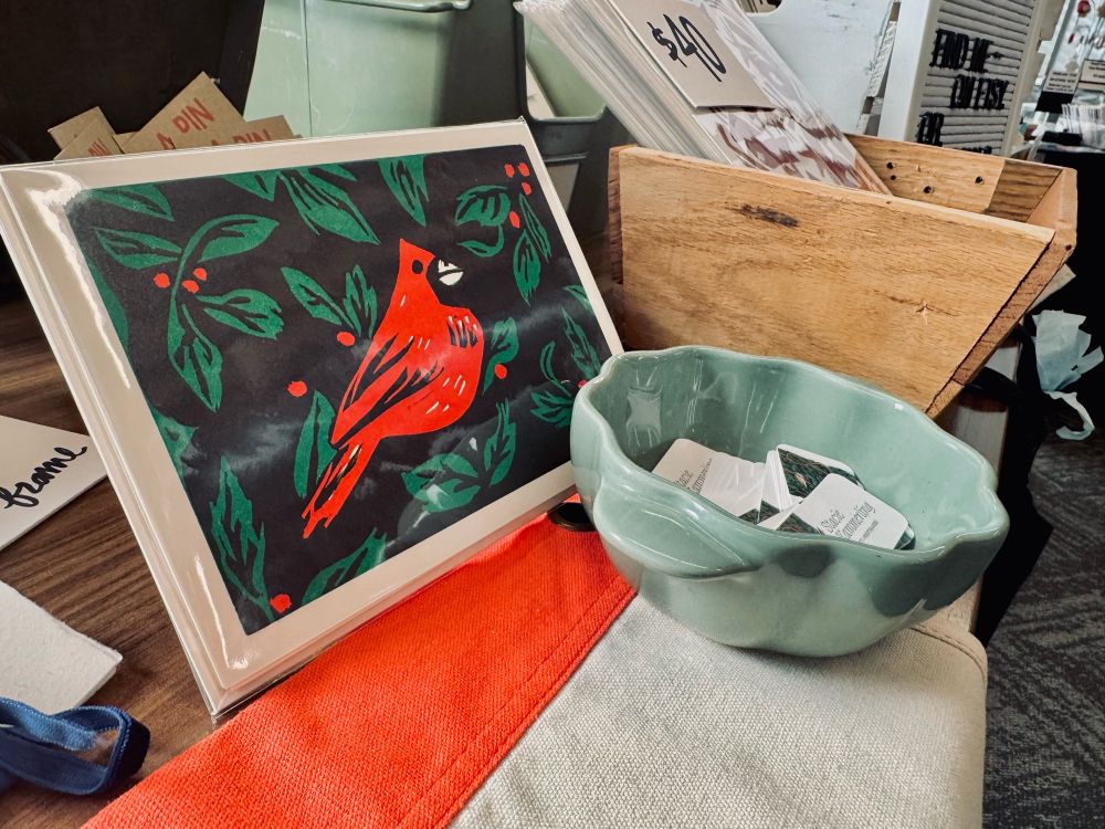 A linocut print featuring a red cardinal sits on a table adjacent to a bowl of business cards
