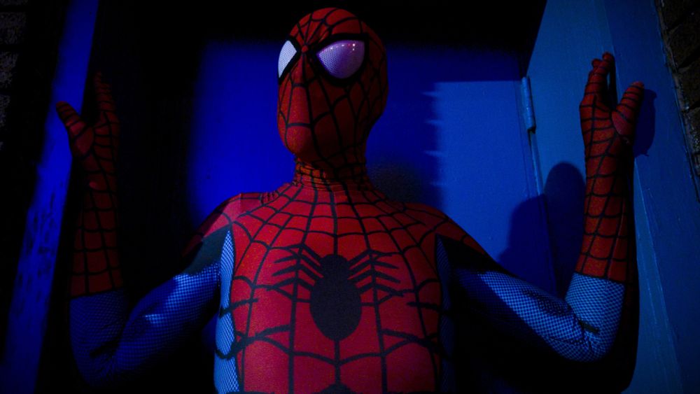 A man posing in a spandex Spider-Man suit.