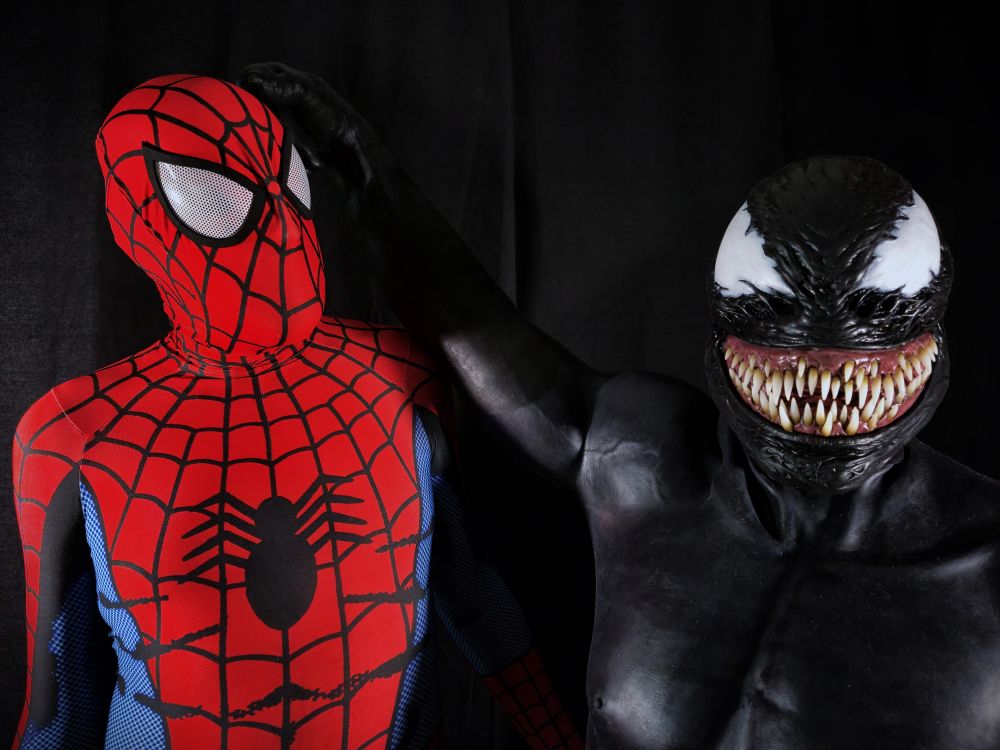 Two men posing in a spandex Spider-Man suit and a silicone Venom suit. 