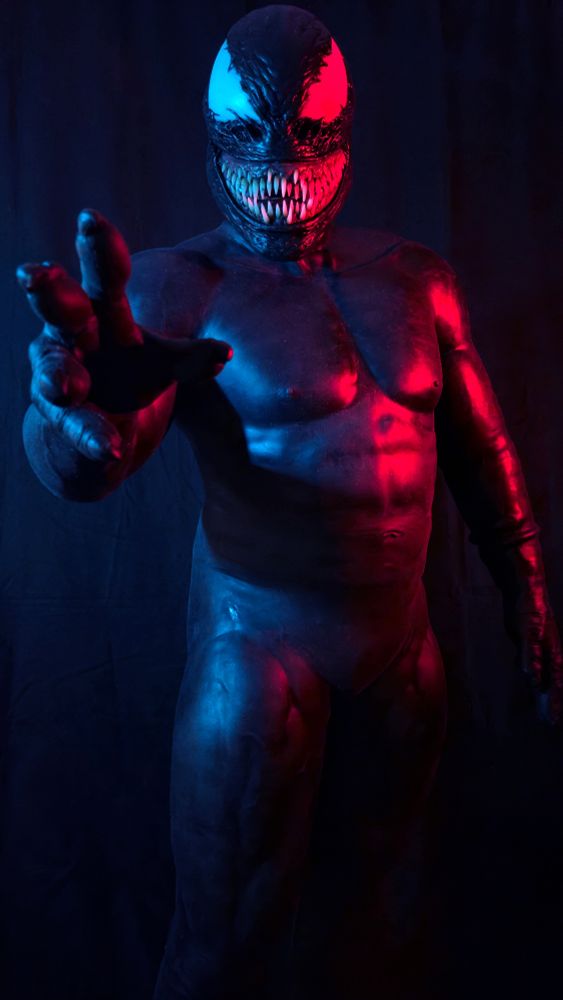 A man posing in a silicone Venom suit and mask. 