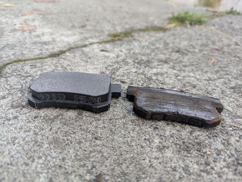 A brand new brake pad sitting next to a sliver of metal that used to be a brake pad