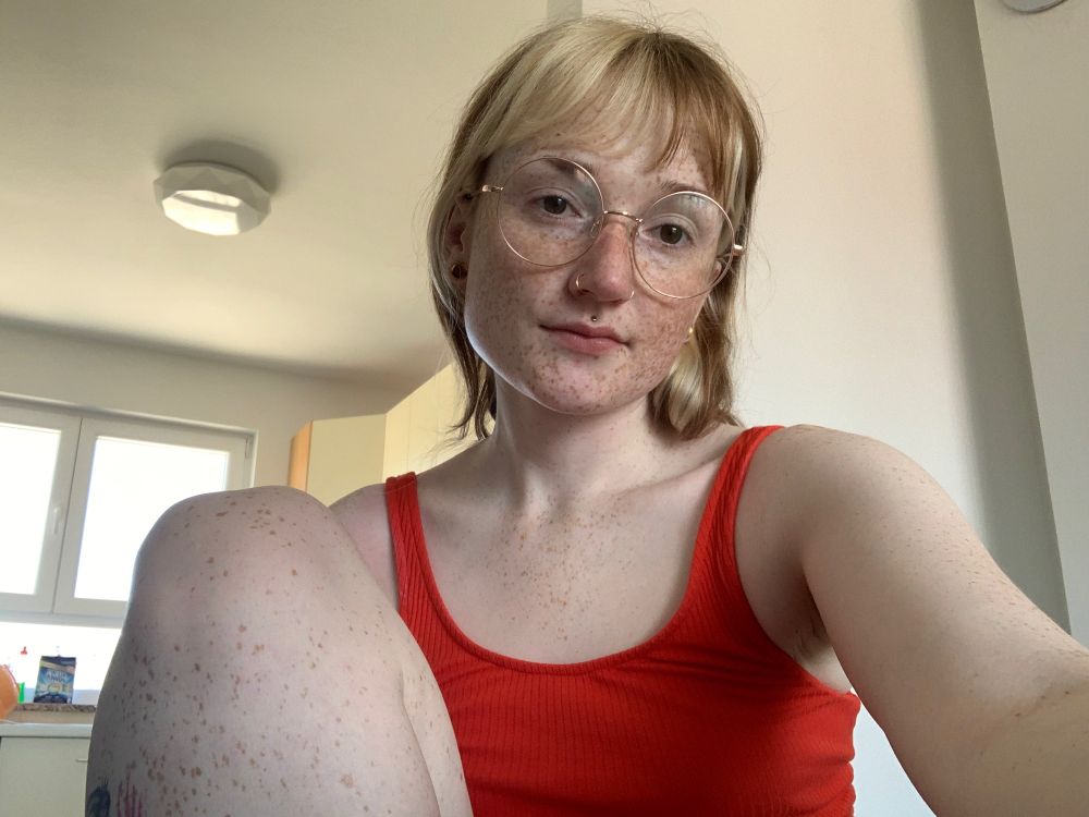 A selfie of me sitting in the dining room wearing a red vest and glasses