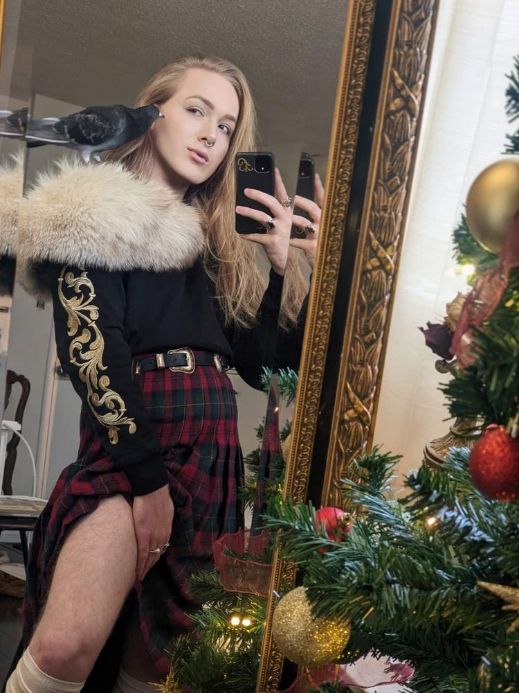 Morningstar is receiving a peck on the cheek from his pet pigeon Hermes as he poses in a tartan skirt and embroidered sweater.