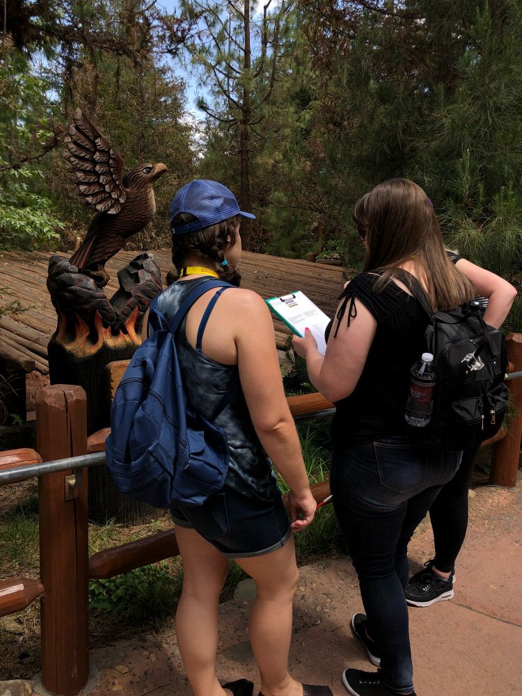 Three people look at a puzzle on a clipboard in front of an eagle statue