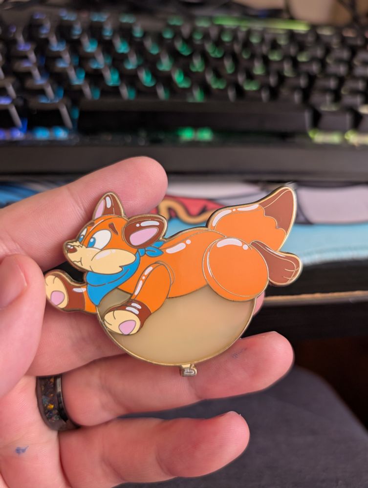A pin of a pooltoy fox with an overinflated belly 