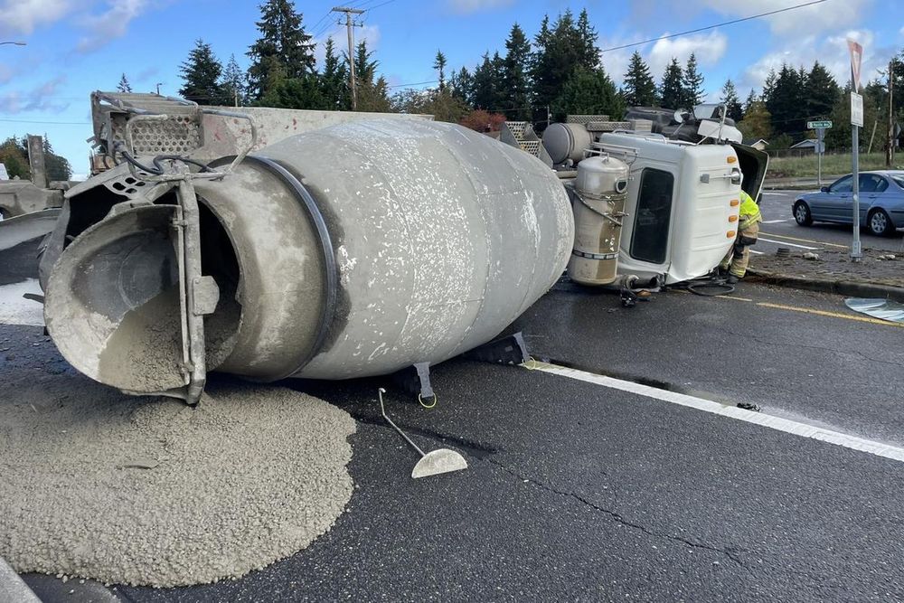 A photo a tipped-over concrete truck with a pile of hardening concrete on the roadway.