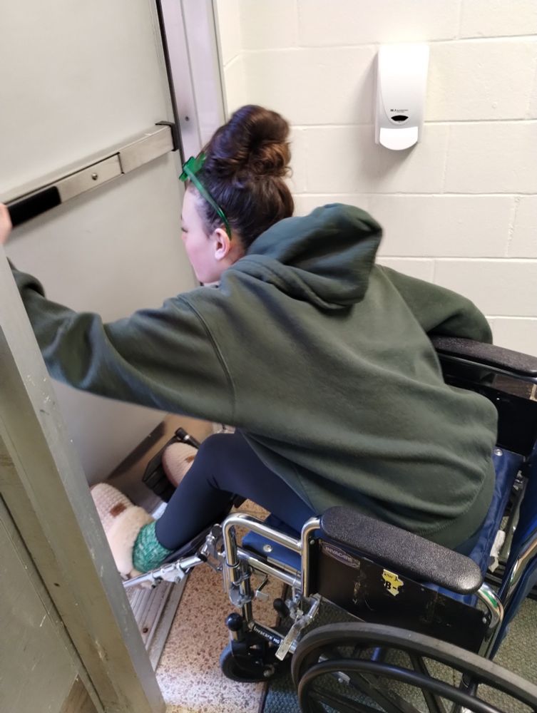Student attempting to open a door while in a wheelchair.