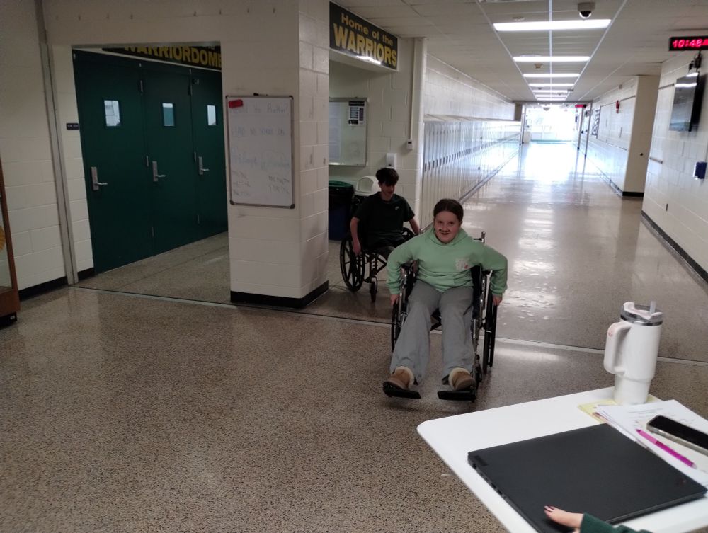 2 students navigating the hallways of a school while in a wheelchair.