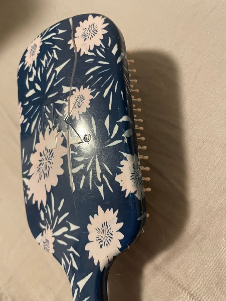 A blue and white hairbrush laying bristles down with a long, deep crack splitting through the hairbrush lengthwise