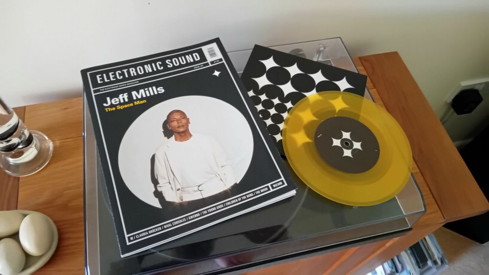 Copy of the latest edition of Electronic Sound magazine featuring Jeff Mills, lay alongside a yellow vinyl special edition 7" single featuring Theme From Star Child. All lay on top of record player.