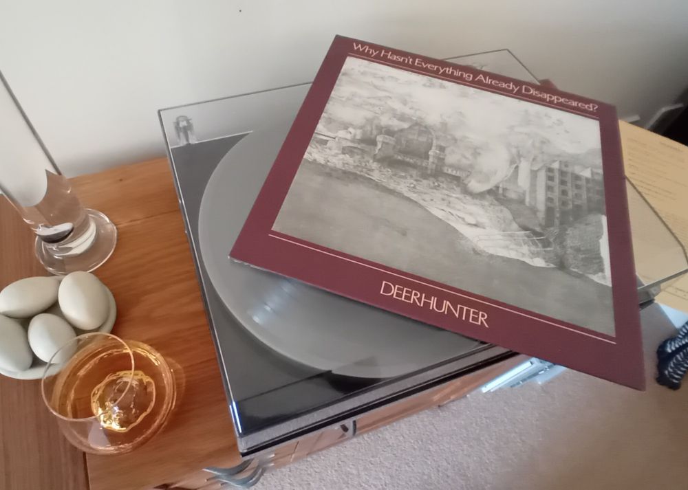 Album cover for 'Why Hasn't Everything Already Disappeared?' by Deerhunter lay on top of record player as record spins underneath. Glass of whisky sat to the side.