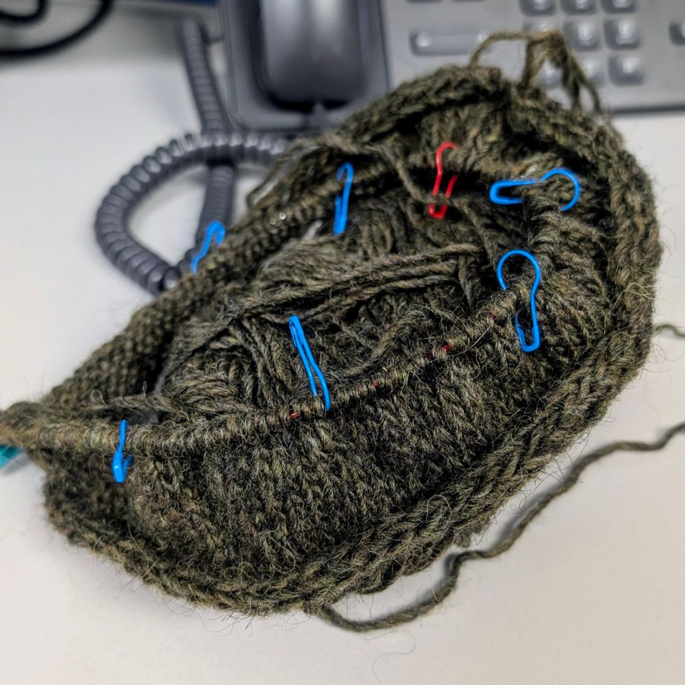 In progress knitting. The yarn is a mossy green color, called "moor" on the website, and there are several stitch markers in it