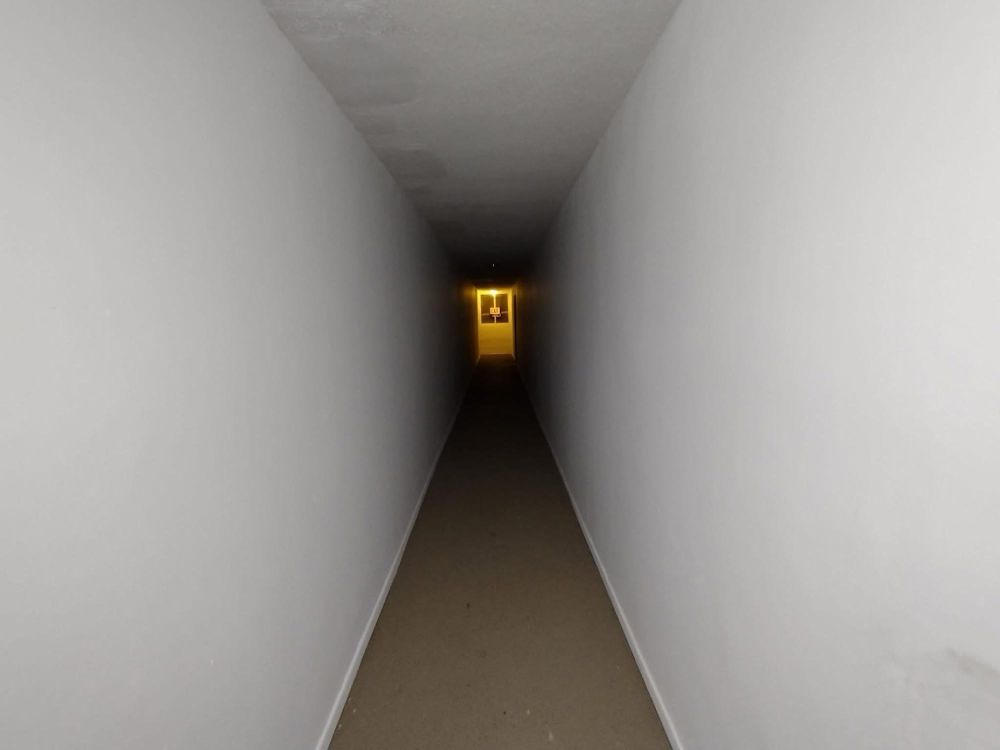 A long, narrow, white corridor leading to a glowing exit.