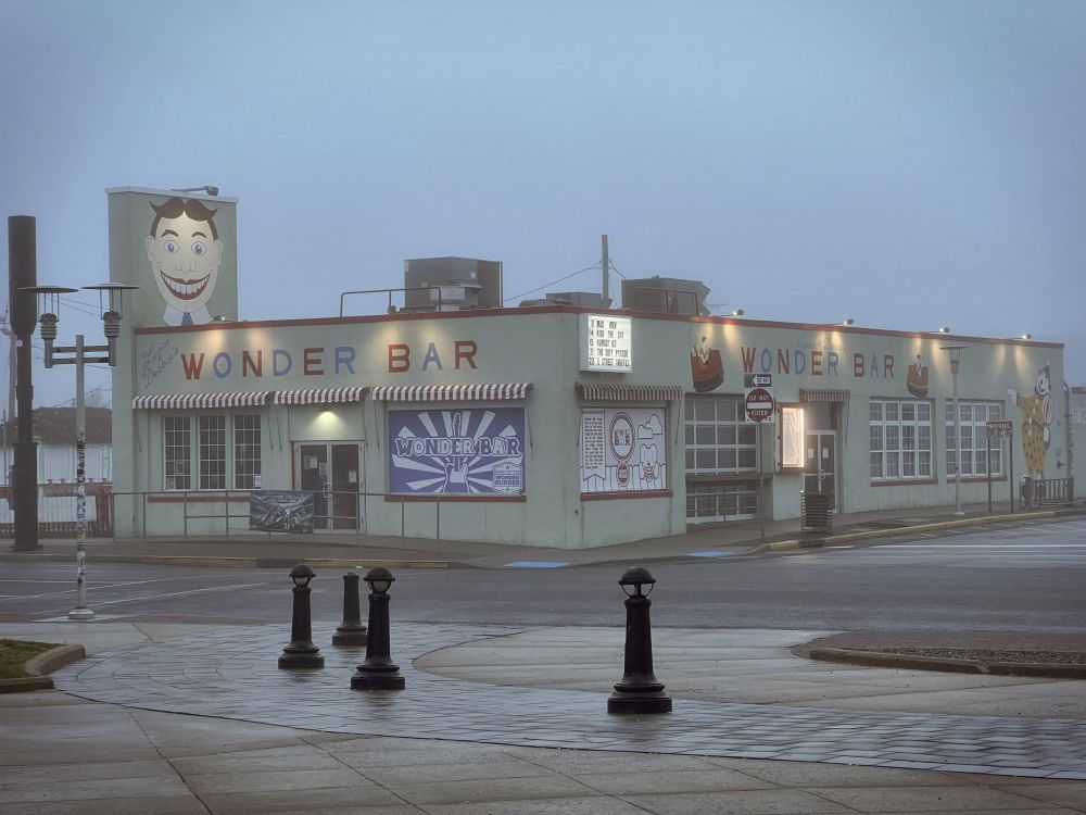A foggy shot of a closed beachside restaurant called Wonder Bar with a disturbingly grin-faced mascot thing and a clown muralled on the wall.