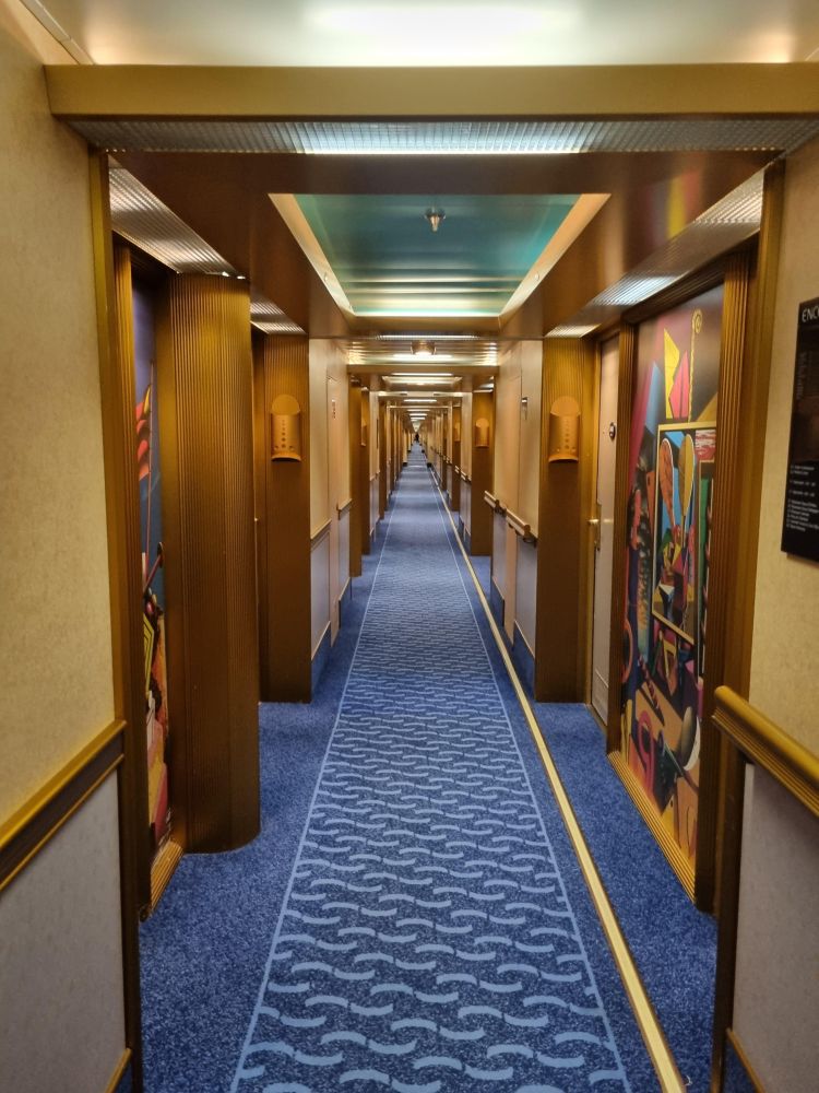 A very, very long corridor of hotel/cruise ship(?) rooms with bright, deco-like designs