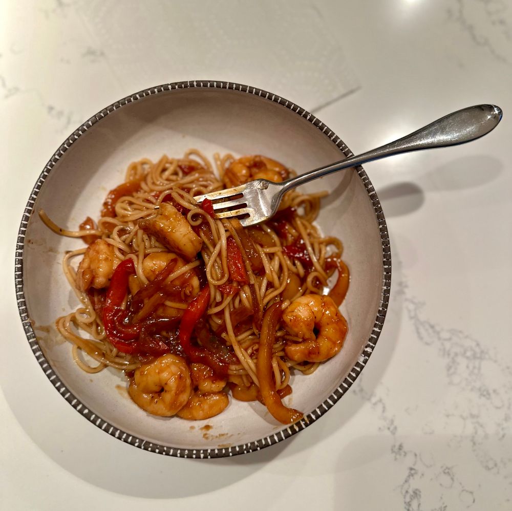 Bowl of deliciousness with a fork in the bowl of peppers, onions, shrimp, and noodles. 