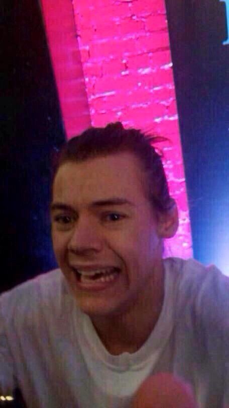 Young Harry Styles with his hair up wearing a white tee. He has a very upset look on his face. 