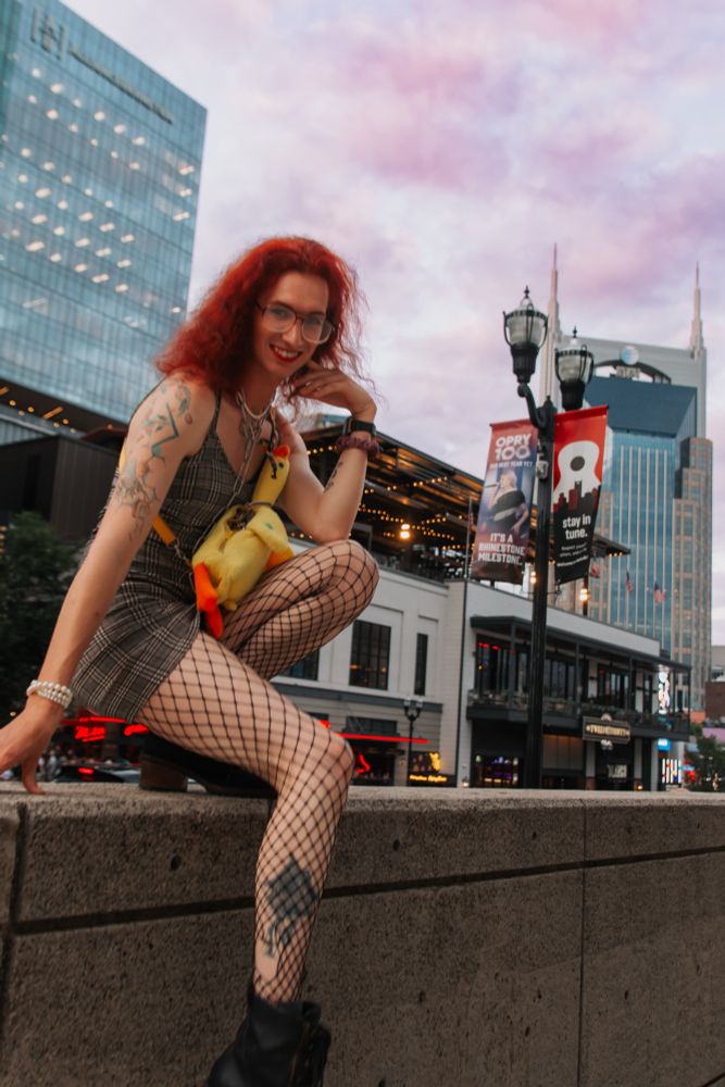 norma jean in a dress and heels and fishnets perched on a concrete wall