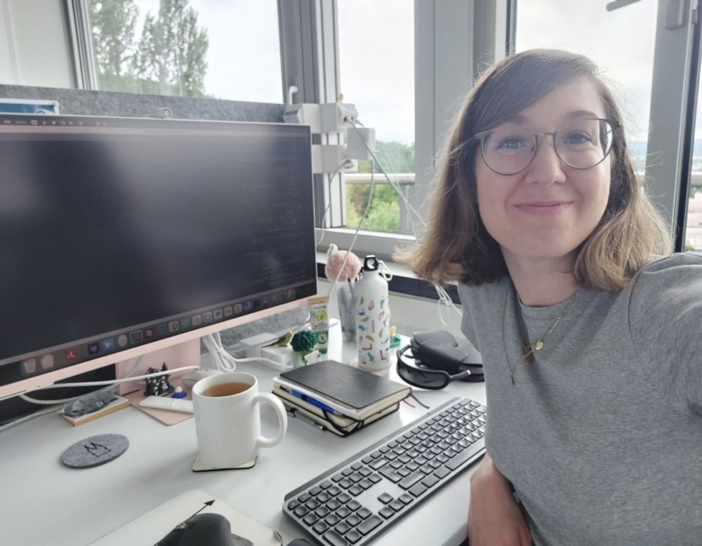A selfie of a woman with glasses at a desk in front of a computer
