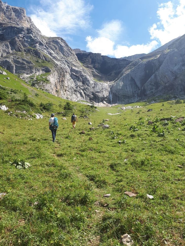 Alpine mountain scene with a cascade and people walking towards it