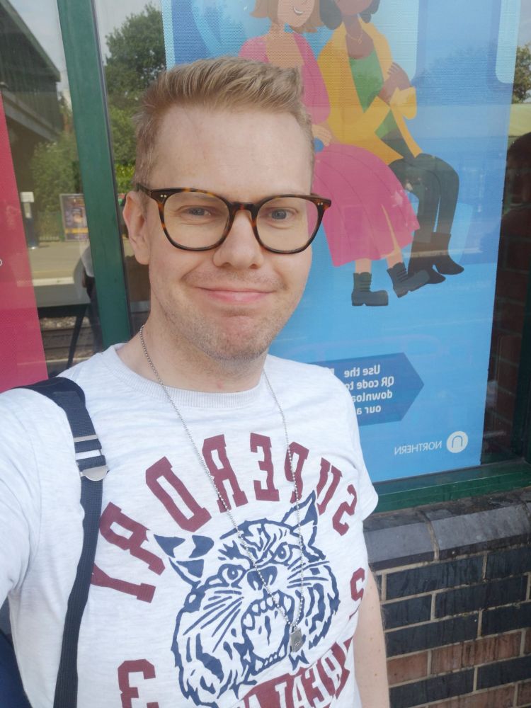 A selfie of me at a train station while wearing a grey Superdry tiger T-shirt.
