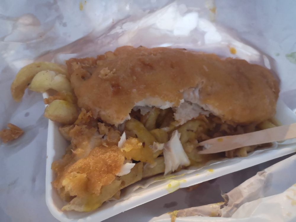 A photo of fish and chips with curry sauce wrapped up in white paper.