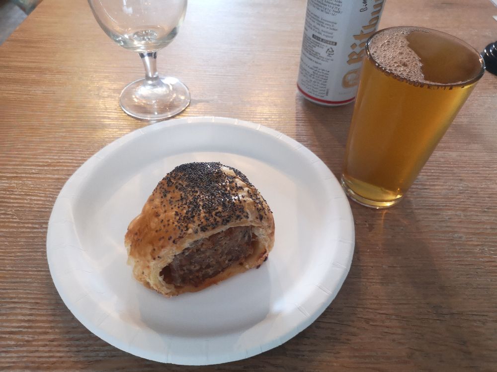 A sausage roll on a paper plate and half pint of beer at The Pangolin.