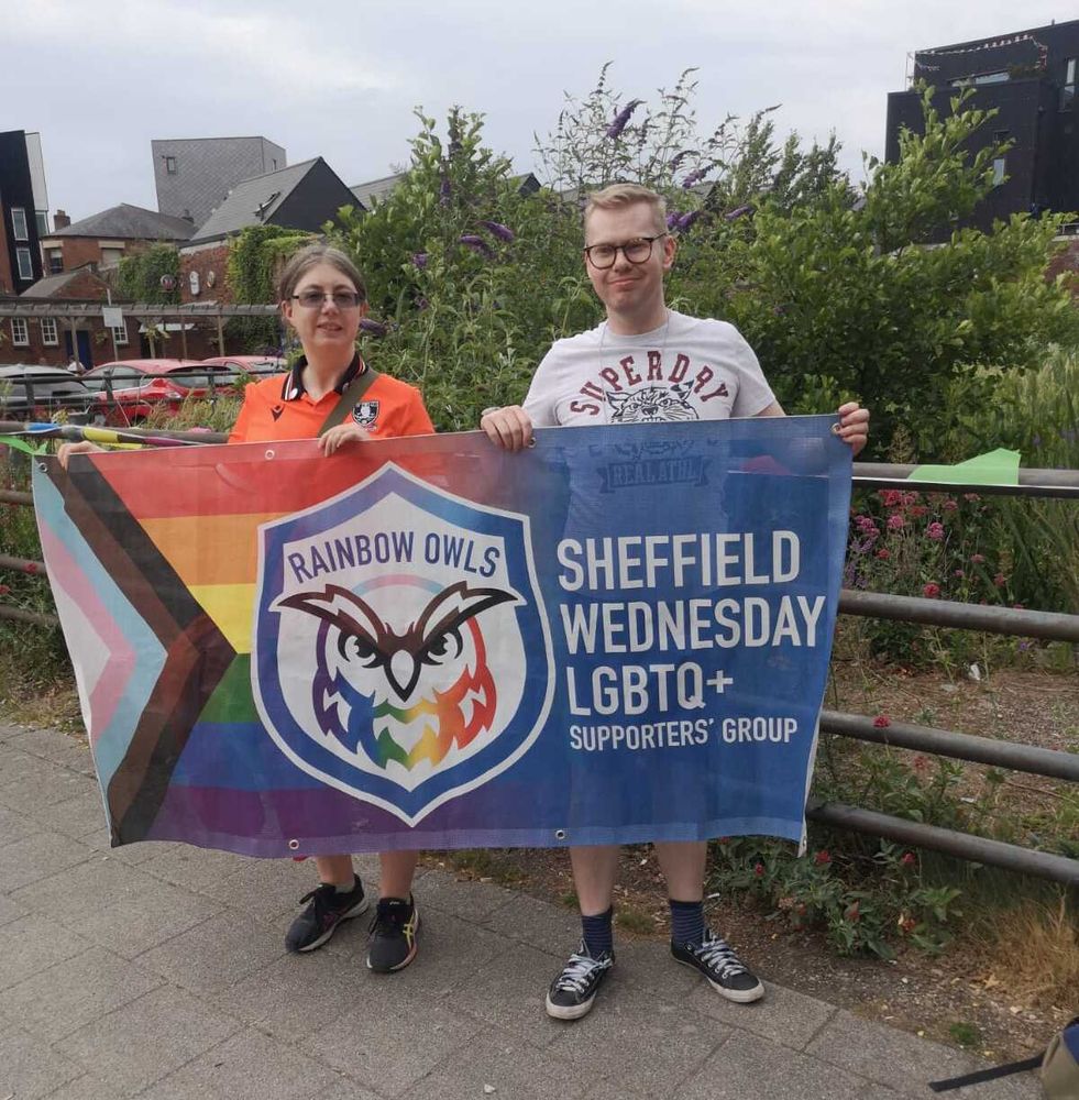 A photo of me holding the Rainbow Owls banner with another member at Kelham Pride.