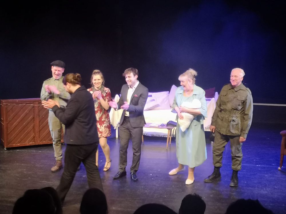 A photo of How Could I Forget? cast members applauding Joe Carnall Jnr from stage at the University of Sheffield's Drama Studio.