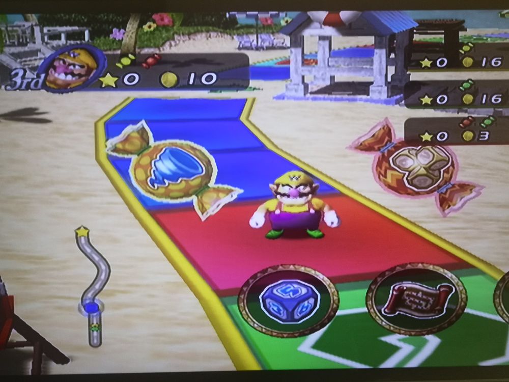 A screenshot of Mario Party 8 on the Nintendo Wii with Wario about to throw the dice on a beach-themed game board.