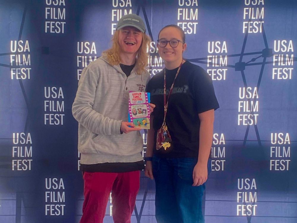 my friend emma and i holding a “kid film” flyer in front of a “usa film festival” backdrop 