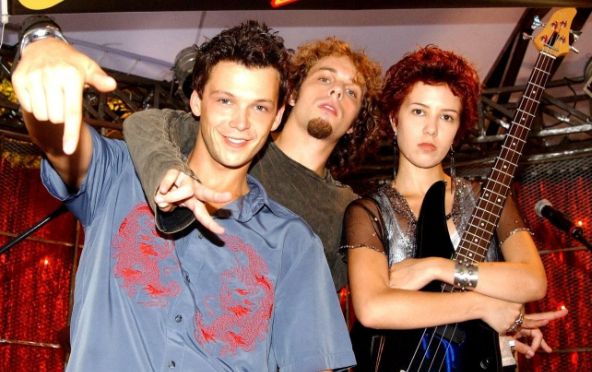 Os atores Guilherme Berenguer, João Velho e Marjorie Estiano na temporada de 2004 de Malhação. Os três vestem roupas descoladas de roqueiros joviais e Marjorie está com uma guitarra na mão, além de microfones no fundo da imagem.