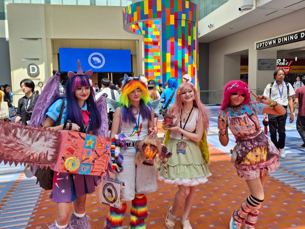 Four cosplayers as My Little Pony characters but bloodied, Rainbow Dash holds a severed head, Twilight has a big chainsaw