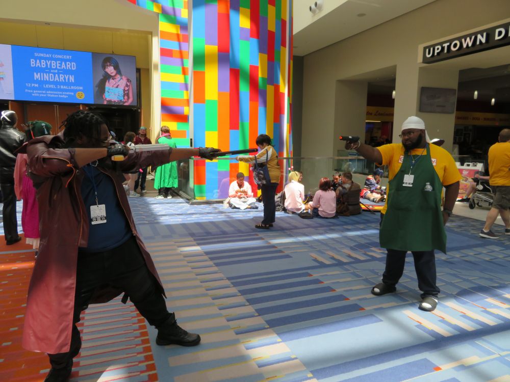 Cosplayer of the titular character from Sakamoto Days pointing a gun at a Dante cosplayer pointing two guns in turn