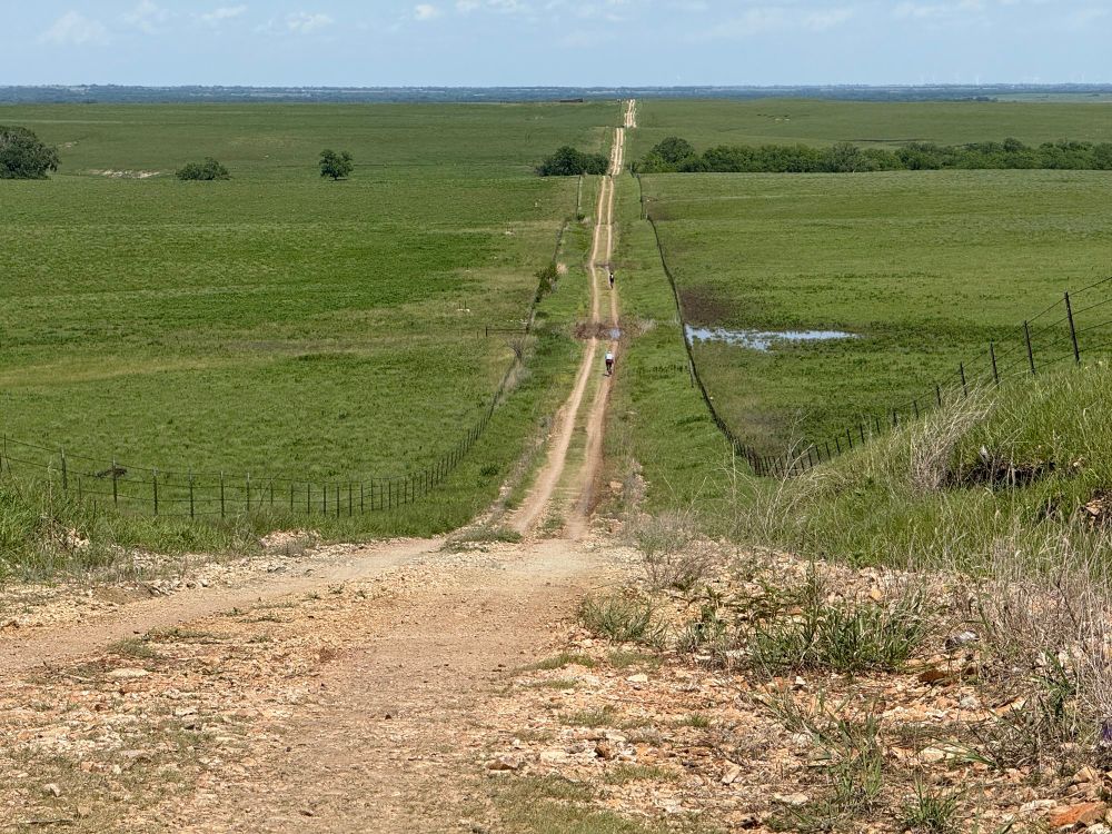 Rollercoaster hills of sharp, chunky gravel and muddy wheel ruts stretch for miles ahead. Cyclists dot the hills to the horizon. The sun blazes