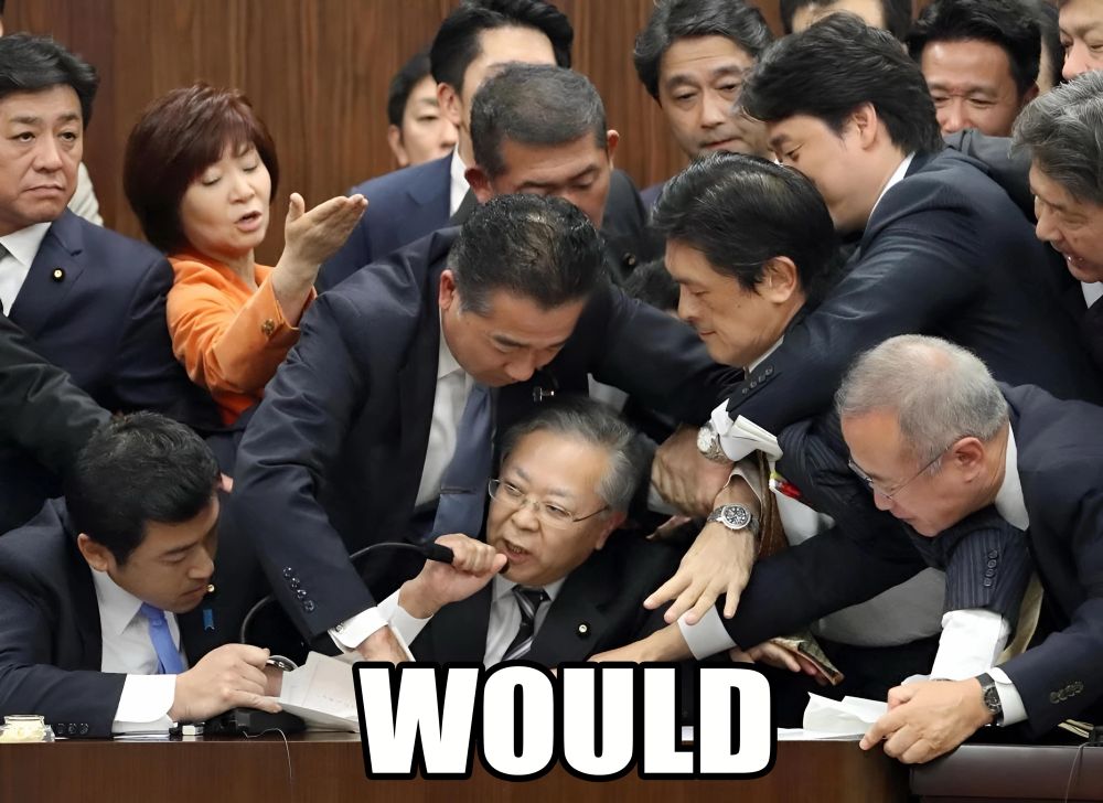 man speaking into microphone saying "would" surrounded by a bunch of people trying to stop him 