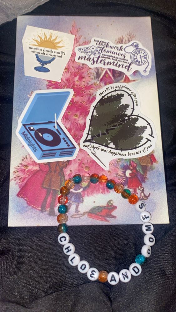 A Christmas card and on top of it is a Taylor swift friendship bracelet and Taylor swift related stickers
