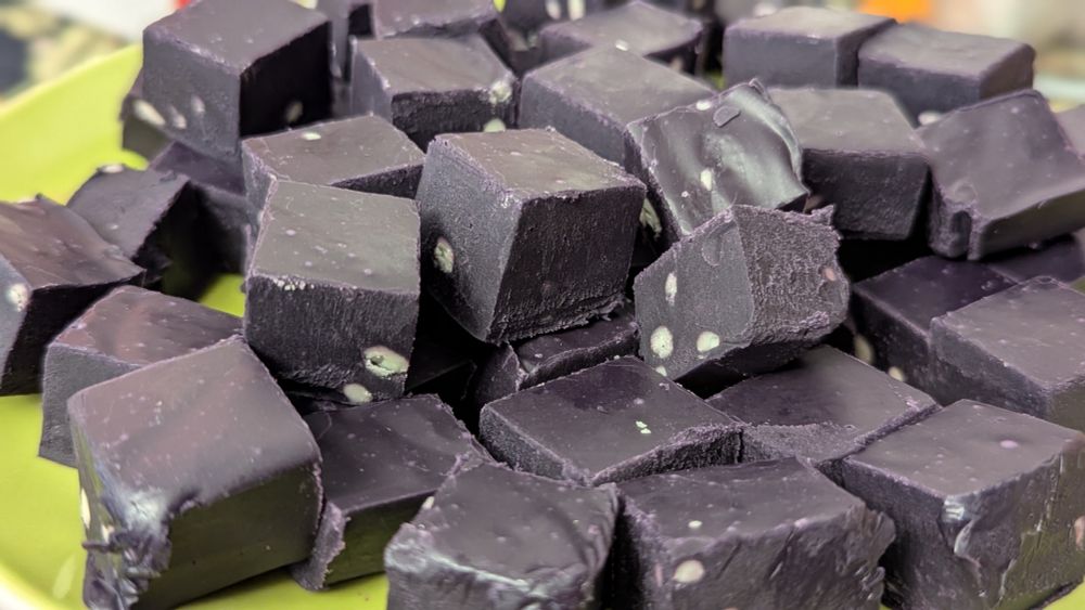 A green plate with cubes of delicious looking fudge. It's a dark purple in color from the ube (a purple yam) it contains