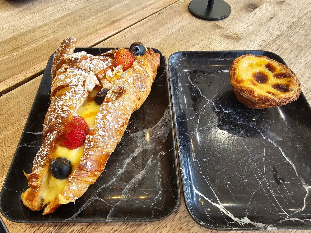 Two black marble coloured plates. The left plate has a custard danish and the right plate has a Portuguese tart.
