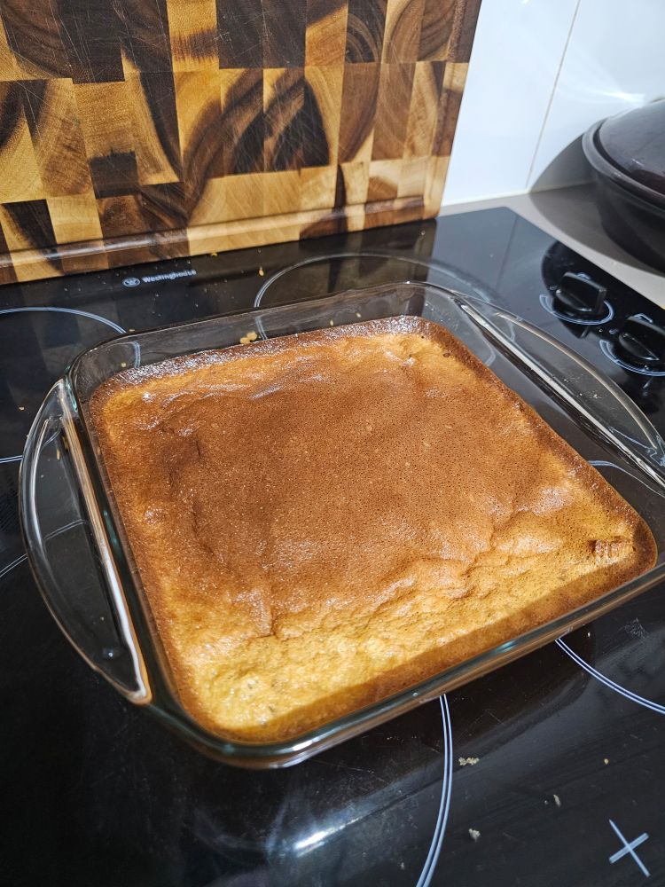 Image shows a square glass baking tray holding a bread pudding-like baked good, sitting on a black stove top.